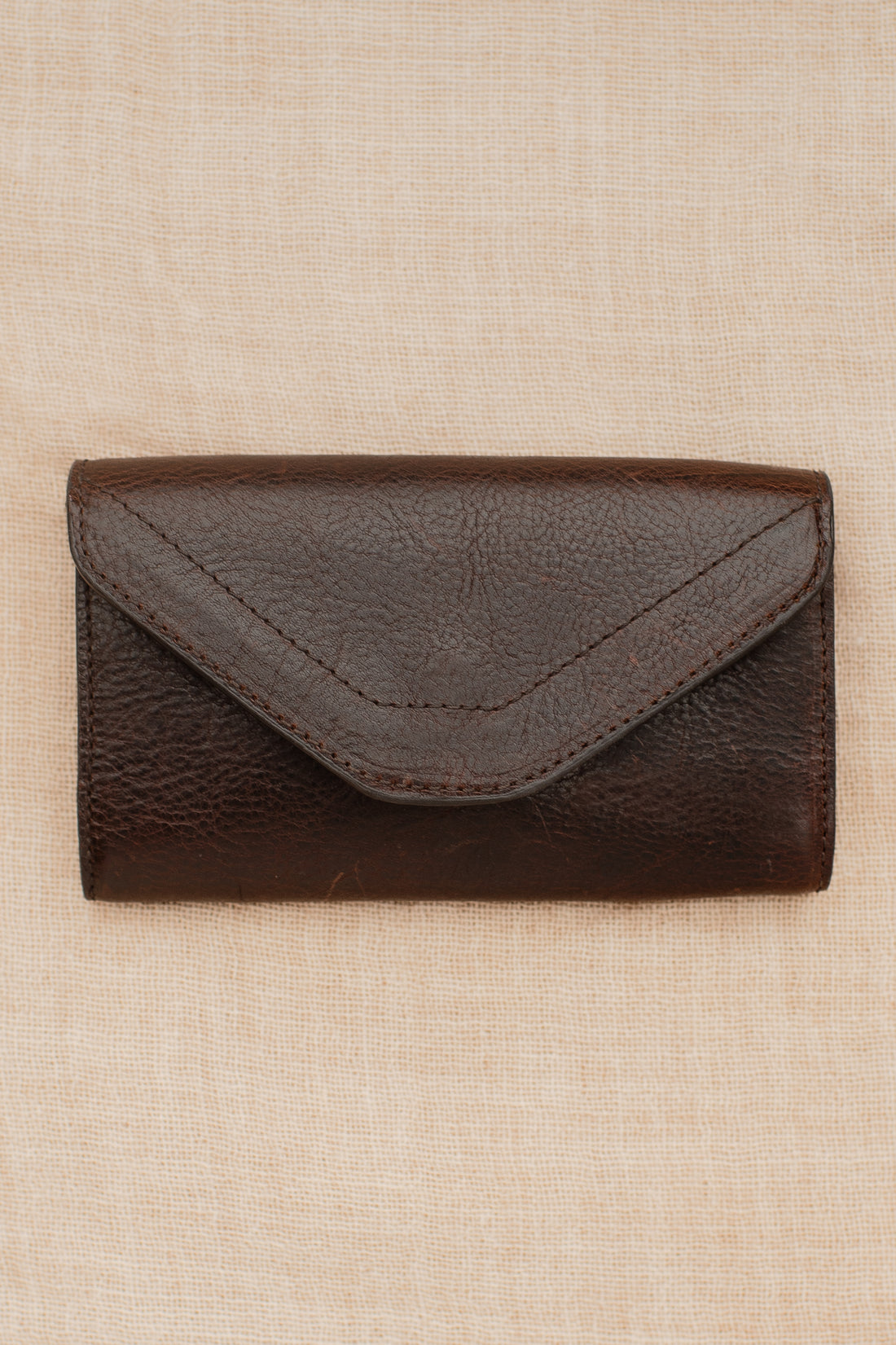 Dark brown pebbled leather equestrian belt bag with envelope-style flap laid flat on neutral fabric background.
