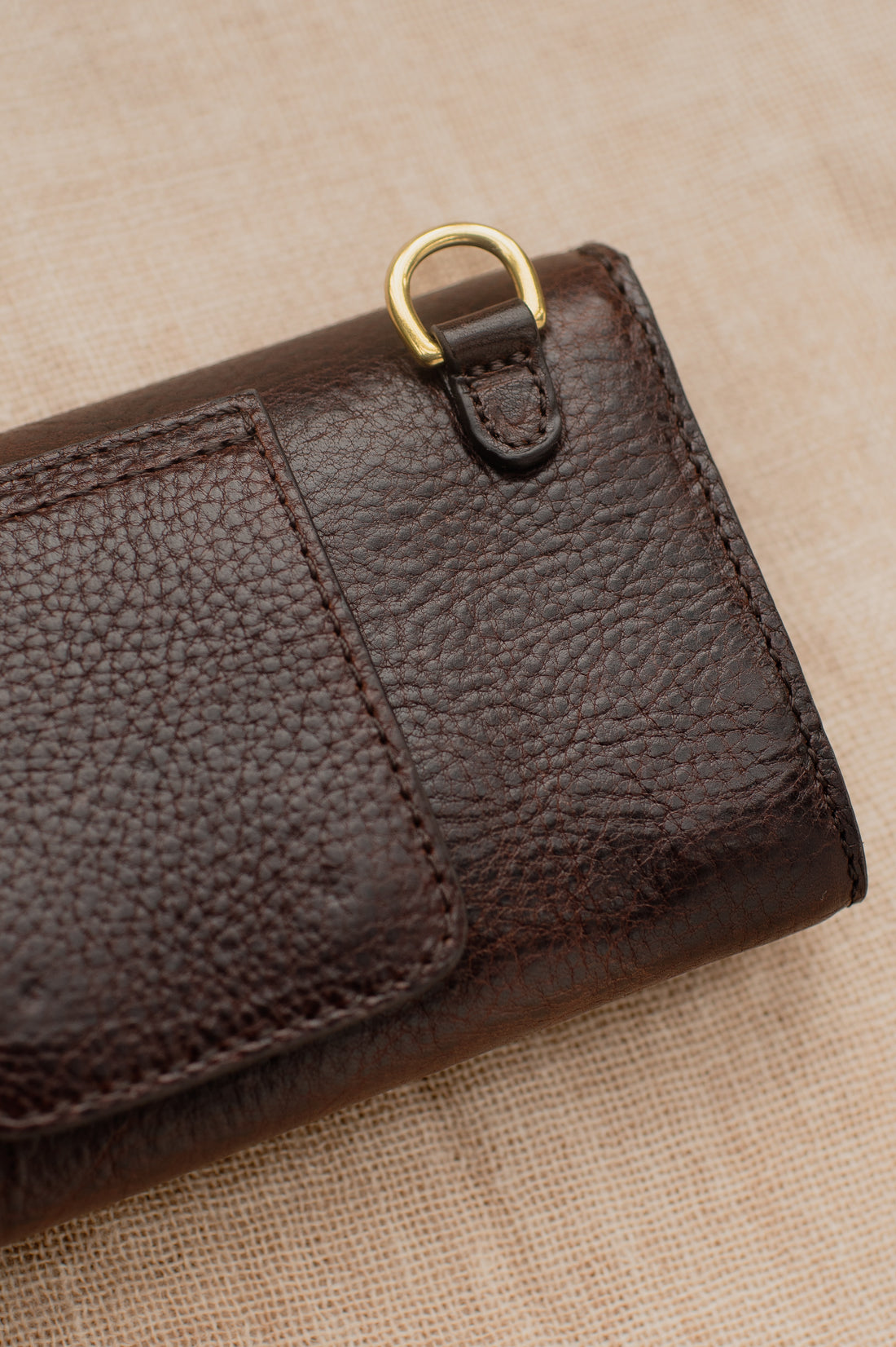 Detail of dark brown leather wallet showing brass D-ring and fine stitching on textured leather with belt strap.