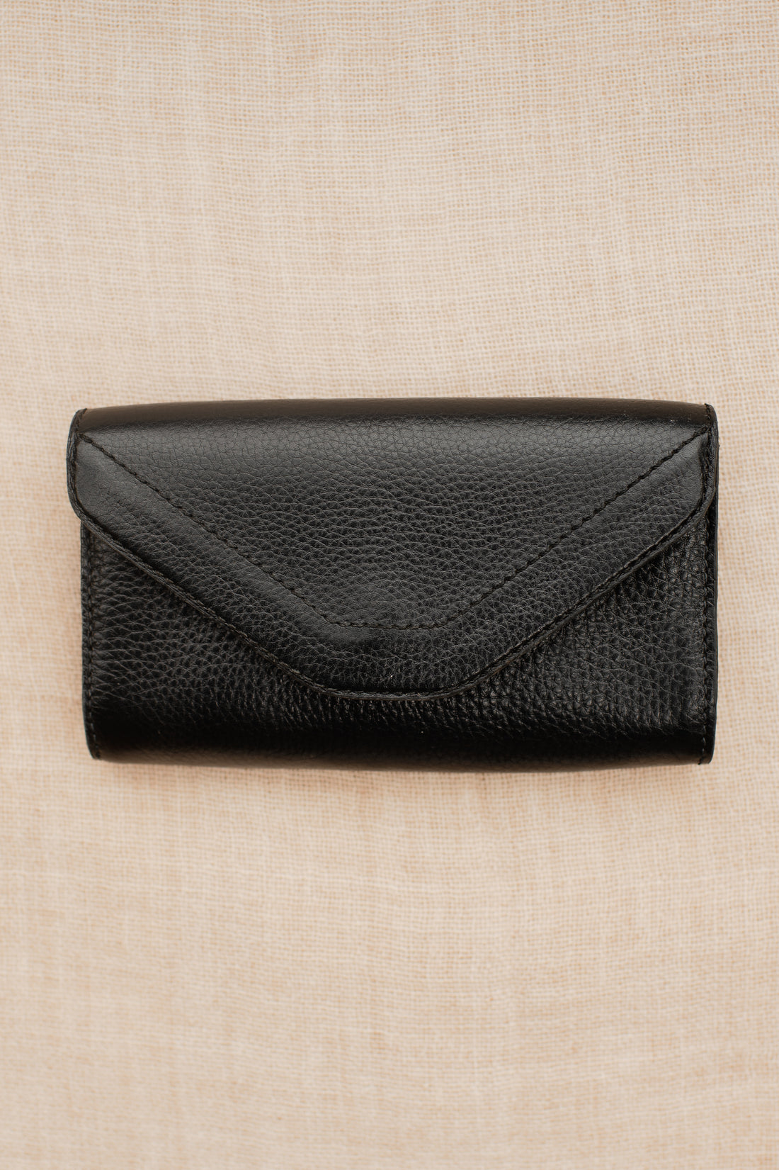 Black pebbled leather equestrian belt bag with envelope-style flap laid flat on neutral fabric background.
