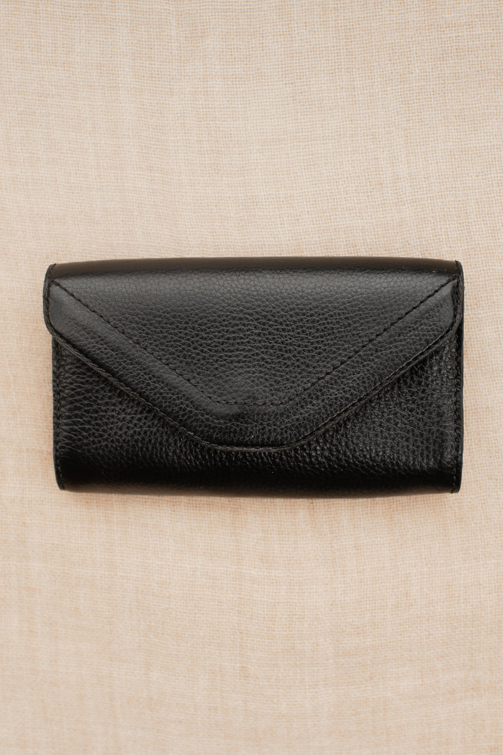 Black pebbled leather equestrian belt bag with envelope-style flap laid flat on neutral fabric background.
