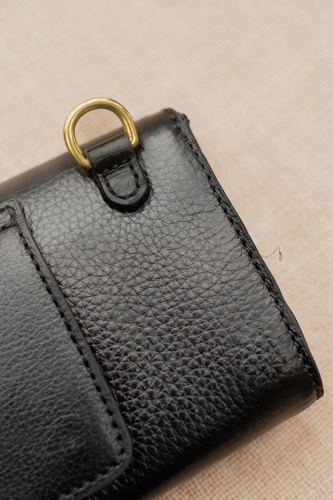 Detail of black leather wallet showing brass D-ring and fine stitching on textured leather.